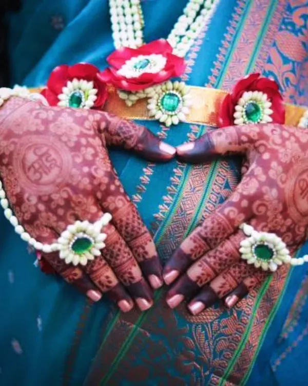 A beautiful baby shower mehendi with the Marathi words 'Aai' (Mother) and 'Baba' (Father) written inside heart shapes. The mother-to-be is wearing traditional floral jewelry, which complements the henna perfectly.