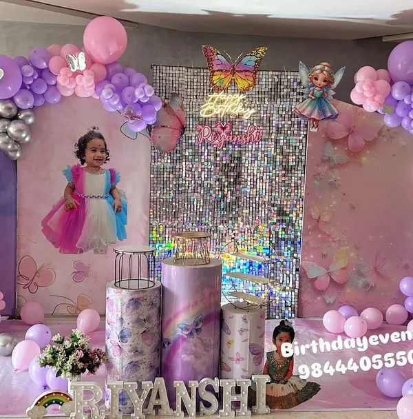A full view of an enchanting butterfly-themed first birthday. This grand setup includes a double balloon arch in pink, purple, and silver, a central shimmer wall, and a personalized backdrop featuring the birthday girl's photo.