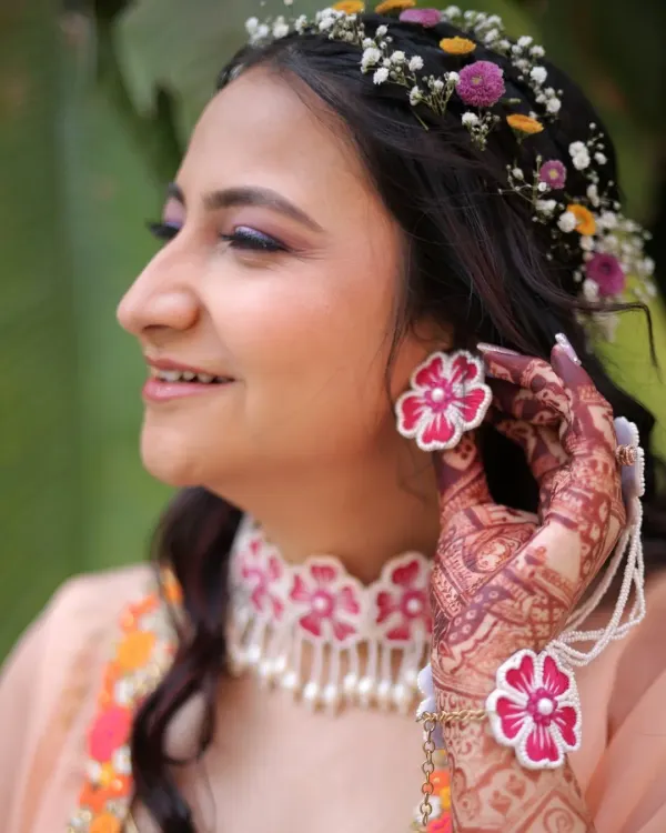 A close-up on the details of a fun Haldi look. The floral jewelry, including the earrings and choker, is the centerpiece, complemented by a pop of purple on the eyes and fresh, glowing skin.