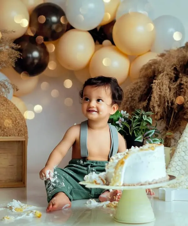 A bohemian-themed cake smash with earthy tones, pampas grass, and soft lights. This little one is just getting started on his delicious cake.