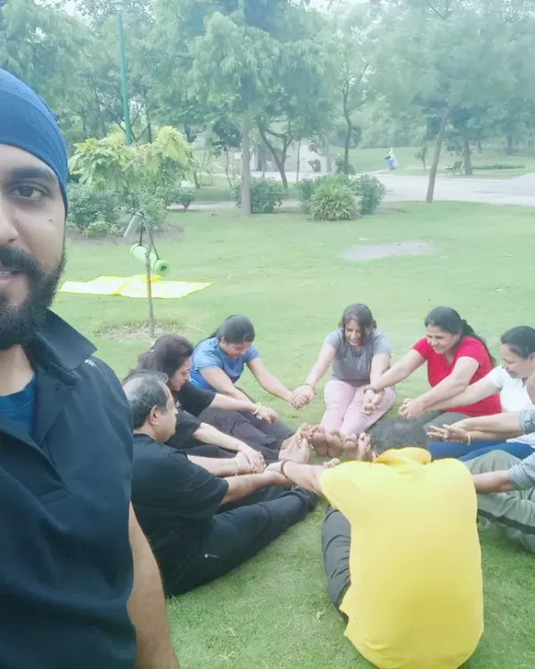 A selfie with my group during an outdoor yoga session. We are practicing a seated forward bend together, enjoying the fresh air and green surroundings.