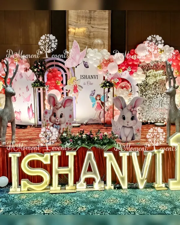 A magical first birthday stage combining winter wonderland and fairy themes. The setup features adorable bunny and reindeer props, a sparkling sequin backdrop, and balloon arrangements in festive red and white, creating a whimsical forest scene.