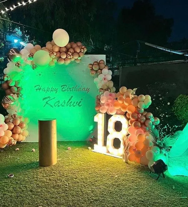 An 18th birthday on a lawn, shown here with green lighting. The setup includes a personalized backdrop and marquee numbers.