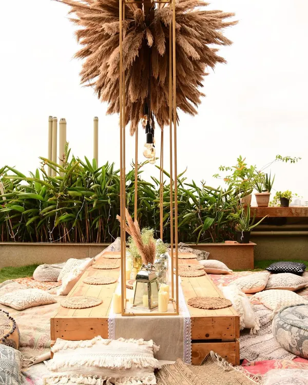 A detailed look at our boho sit-down arrangement. The centerpiece is a tall metal structure filled with pampas grass, with Edison bulbs hanging down to light the low wooden table.