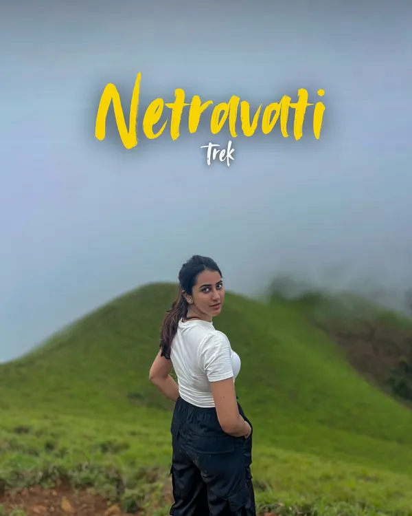 A trekker posing at Netravathi Peak, with the name of the trek overlaid. This is the picture perfect moment you'll want to capture.