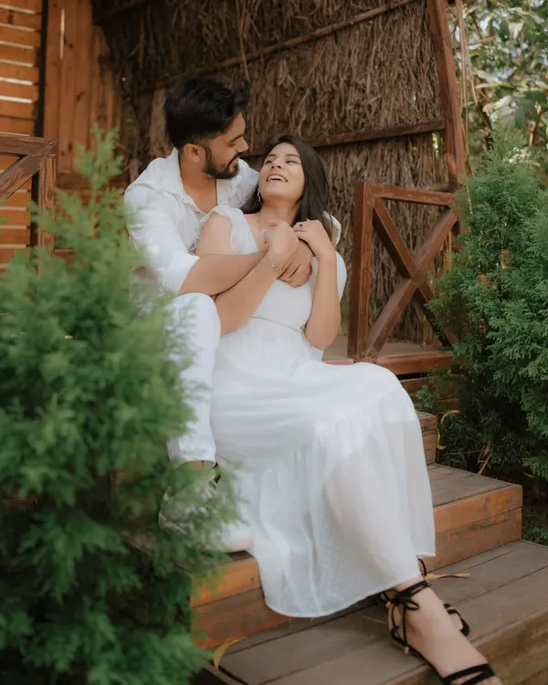 A moment of pure, uninhibited laughter on a rustic wooden porch. Dressed in coordinated white, this couple's joy is infectious, showcasing a perfectly candid moment from their pre-wedding shoot.