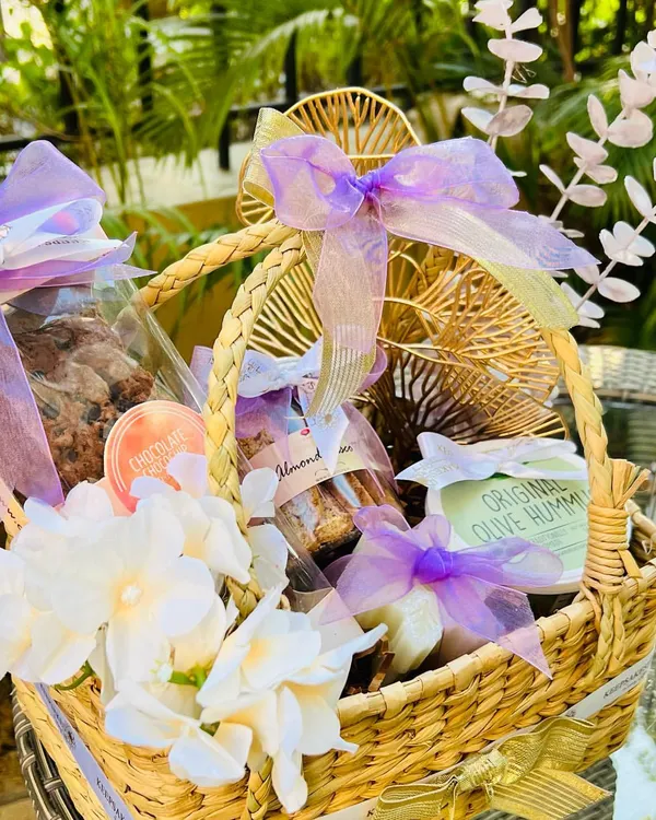 A custom hamper designed with a lilac and lavender color scheme. This woven basket is filled with almond biscotti, hummus, and cookies, and beautifully decorated with white flowers, dried lavender sprigs, and delicate purple ribbons.