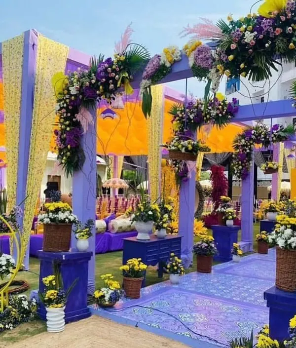 A stunning Haldi ceremony setup featuring a unique purple and yellow color scheme. We used lush floral arrangements and elegant draping to create a modern yet festive look for this outdoor event.