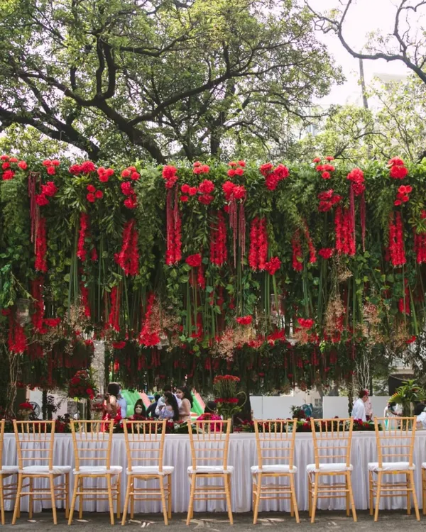This stunning overhead installation features a dense canopy of hanging red florals and lush greenery. It completely transforms an outdoor dining area, creating a dramatic and luxurious atmosphere for a corporate luncheon or gala dinner.