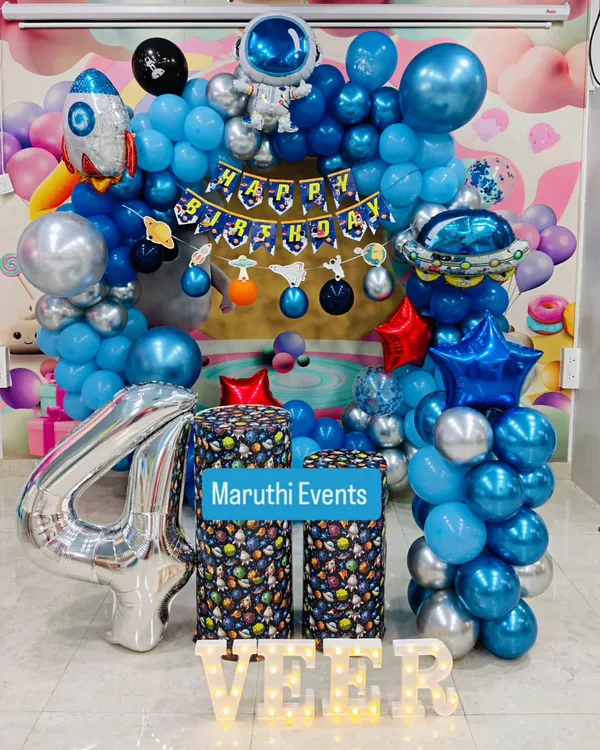 An out-of-this-world space theme for Veer's 4th birthday. This setup includes a balloon arch with astronaut and rocket ship foil balloons, themed plinths, and a large silver number '4'.