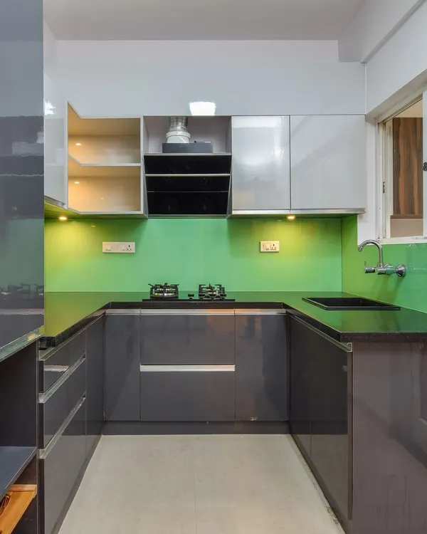 A U-shaped modular kitchen with glossy grey cabinets and a vibrant green backsplash. This design maximizes counter space and storage, with everything easily within reach for an efficient cooking experience.