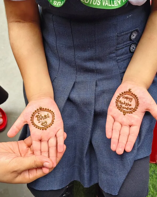 A simple and sweet Rakhi design for a little girl. One palm says 'Bhai' with a heart, and the other says 'Happy Raksha Bandhan'.