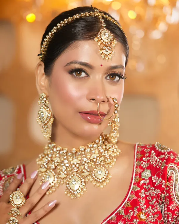 A classic bridal look featuring a heavy Kundan choker and matching earrings, maang tikka, and nath. This complete set provides a majestic feel, perfect for your main wedding ceremony.