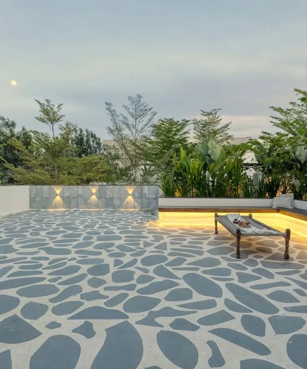 The spacious seating area of the Santorini-style terrace at dusk. The custom flagstone flooring, built-in bench with strip lighting, and surrounding greenery create a perfect ambiance for evening relaxation.