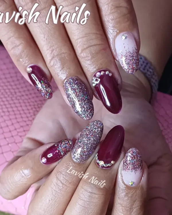 A dramatic set of almond nails combining deep burgundy, full-coverage holographic glitter, and a glitter fade with rhinestone details.