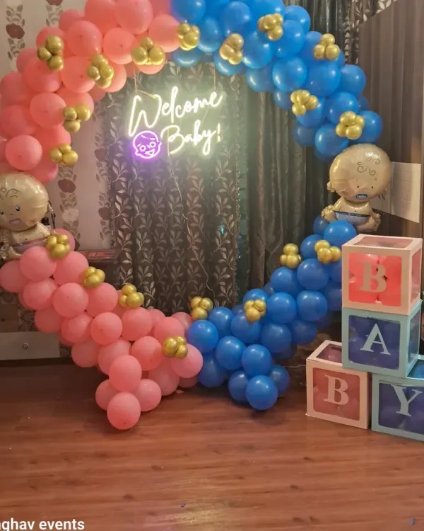 A beautiful circular balloon arch in pink and blue, perfect for a gender reveal or baby shower. This setup includes a "Welcome Baby" neon sign, baby-themed foil balloons, and transparent 'BABY' blocks.