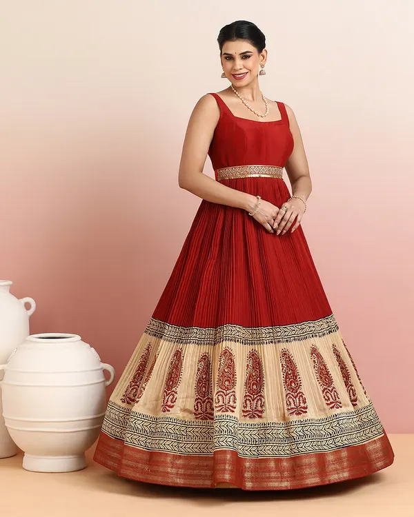 A masterpiece of grace, this regal red and beige gown features a finely pleated bodice and a skirt adorned with ornate paisley embroidery. The shimmering golden zari border adds a touch of heritage charm.