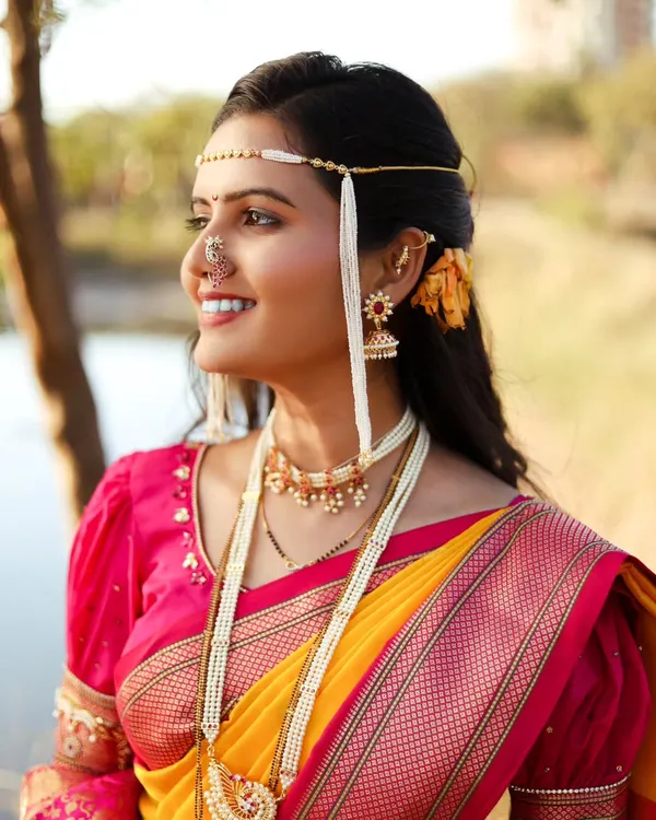 A radiant close-up of a woman in a yellow and pink Nauvari saree, adorned with traditional Maharashtrian bridal jewelry, including the distinctive Mundavalya.