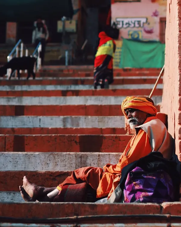 A sadhu rests on the steps of the ghats in Varanasi, his vibrant orange robes contrasting with the weathered stairs. This image captures a moment of peaceful solitude, a common sight in a city that is constantly moving yet full of stillness.