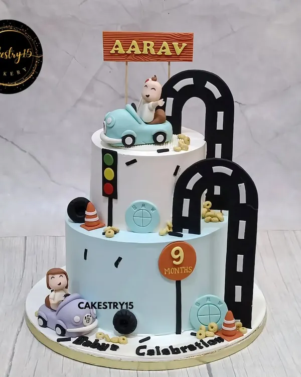 A playful two-tier car-themed cake for a 9-month milestone. This 4kg black forest cake features fondant cars and a winding road design for a fun and adventurous celebration.