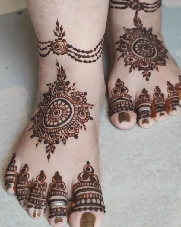 An elegant foot design featuring a central mandala and a delicate chain anklet. The toes are also beautifully decorated, creating a look that is both traditional and chic.