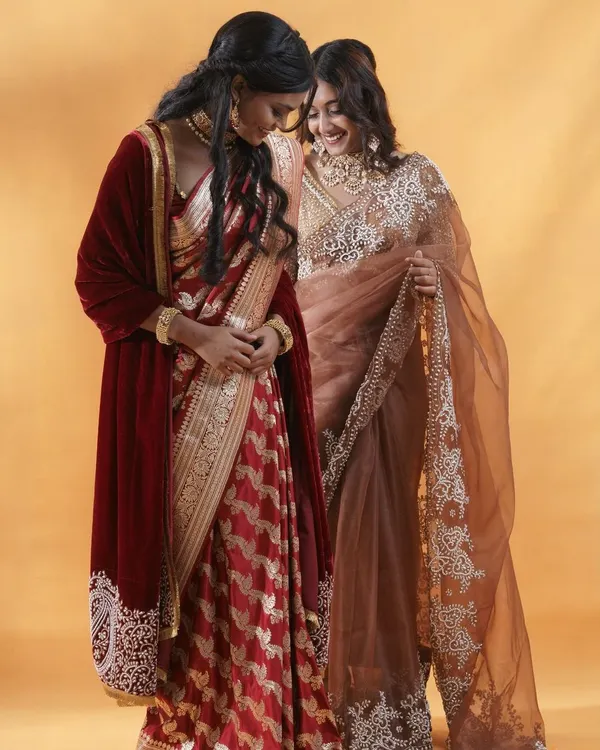 This shot captures the beautiful interaction between two models, showcasing different sarees from the same collection. The warm lighting and joyful expressions create an image that feels both elegant and authentic, perfect for a brand lookbook.