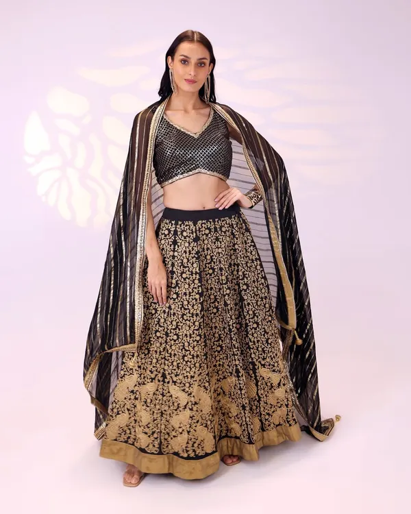 This black and gold lehenga is a timeless choice for a bridesmaid or wedding guest. The skirt features intricate gold embroidery, paired with a shimmering blouse and a striped dupatta that adds a modern touch.