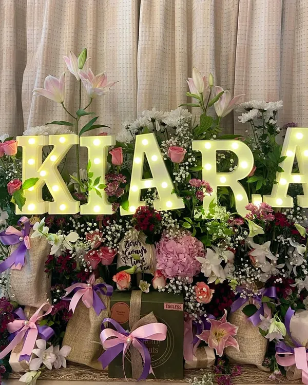 Celebrating a birthday should be as unique as the person themselves. This stunning floral hamper, personalized with the name 'Kiara' in glowing marquee letters, is designed to be an unforgettable centerpiece for any celebration.
