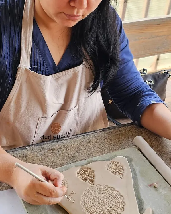 A student in a corporate workshop carefully carving intricate patterns into a clay slab. Hand-building allows for so much creativity and detail.