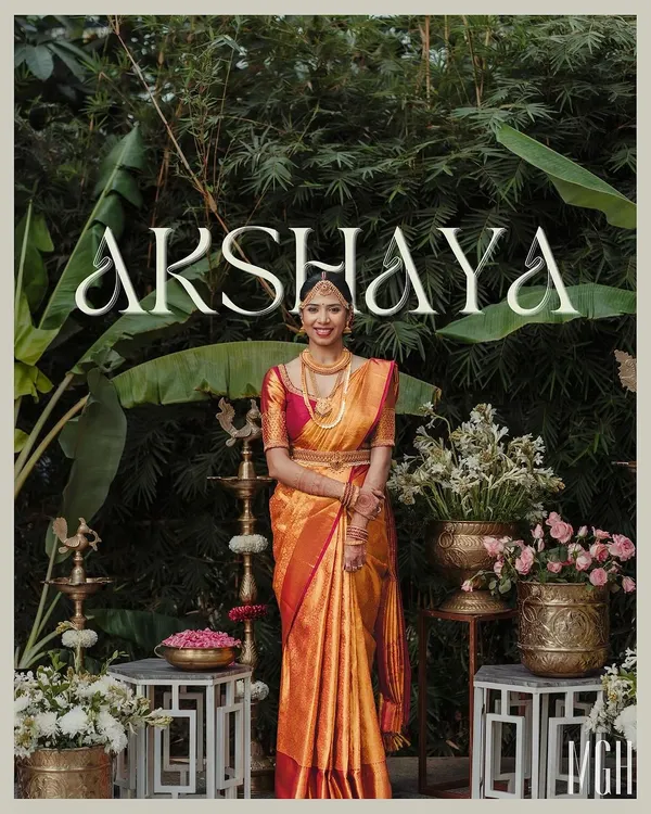 A beautiful bride stands before our traditional South Indian photo booth, complete with brass lamps, banana plants, and classic floral arrangements.