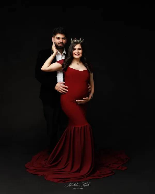 A regal maternity portrait for a queen awaiting her heir. The rich red gown and crown create a powerful, dramatic look against a classic dark backdrop.
