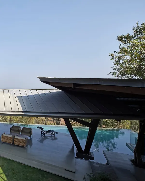 The Lateral Verandah House features a dramatic roofline that mirrors the stepping terrain. A bridge-like structure connects different parts of the home over the infinity pool.