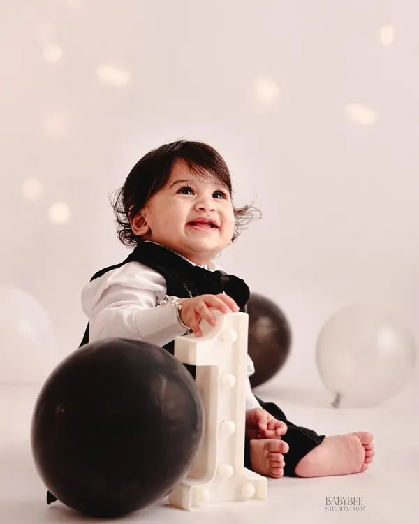 A simple and classic first birthday portrait. The glowing number '1' prop and a happy smile are all that's needed to mark this special milestone in a timeless way.
