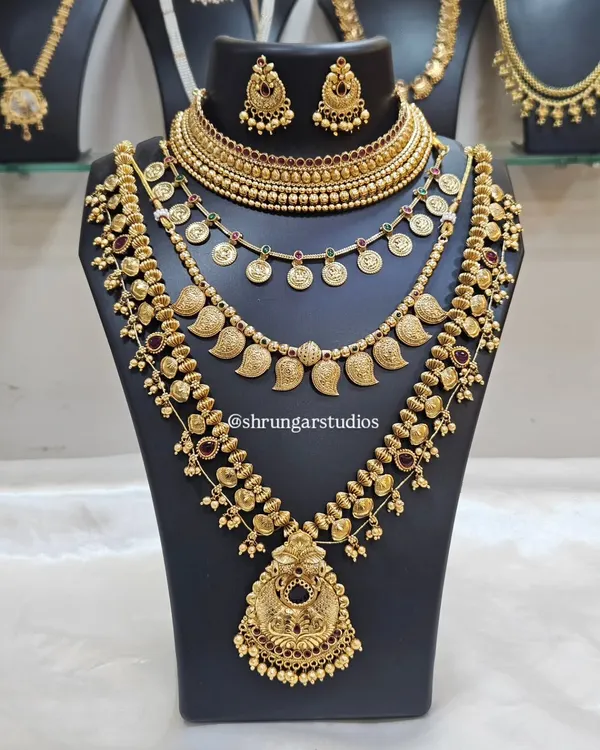 This is the complete Maharashtrian bridal look you've been dreaming of. This layered set features a traditional choker, a coin necklace (putli haar), a mango-motif haar, and a longer, grand temple-style necklace, all in a rich antique gold finish. It's perfect for the bride who wants a truly royal and authentic 'Navari' look.