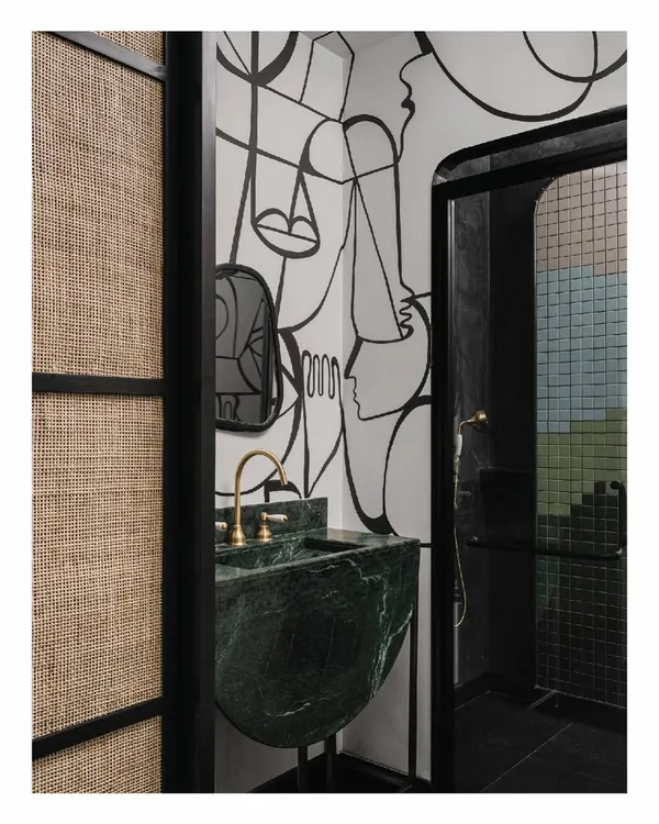 This bathroom in the 'Aria' project is a continuation of the home's artistic narrative. A hand-painted mural flows into a dark, cave-like shower space, while a custom-carved green marble sink stands as a functional sculpture.