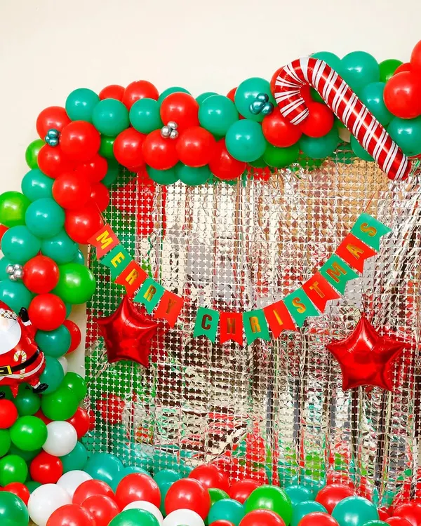 We designed this vibrant Christmas party photo corner, featuring a classic red and green balloon arch. The shimmering silver foil curtain backdrop, candy cane, and Santa Claus foil balloons complete this festive decoration, perfect for home or office celebrations in Bangalore.