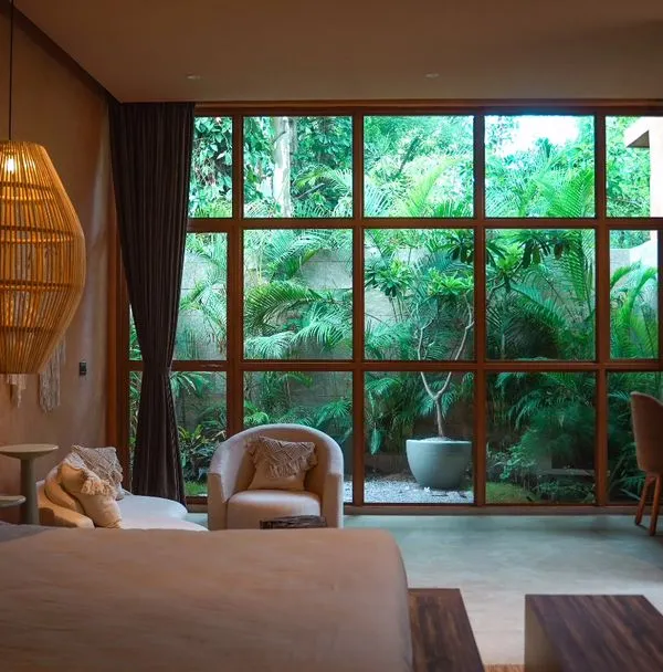 Unwind in the lap of luxury in one of my premium suites, featuring earthy tones and a large window with a garden view.