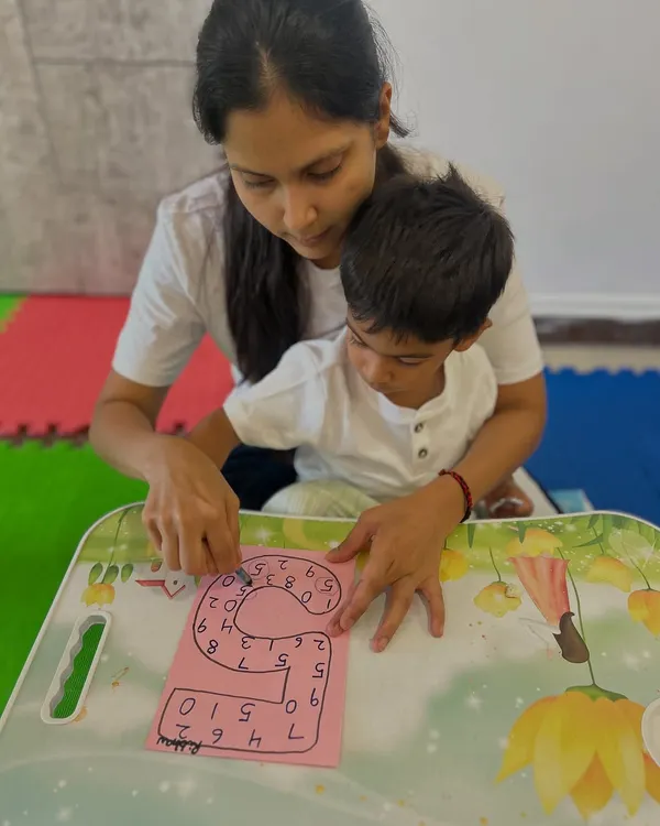 A mother and child work together on a number tracing worksheet. This guided activity helps with number recognition and pre-writing skills.