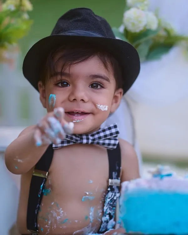 The best part of a cake smash is getting your hands messy. This close-up shot captures the pure joy and curiosity of a first birthday celebration, complete with a stylish bow tie and suspenders.