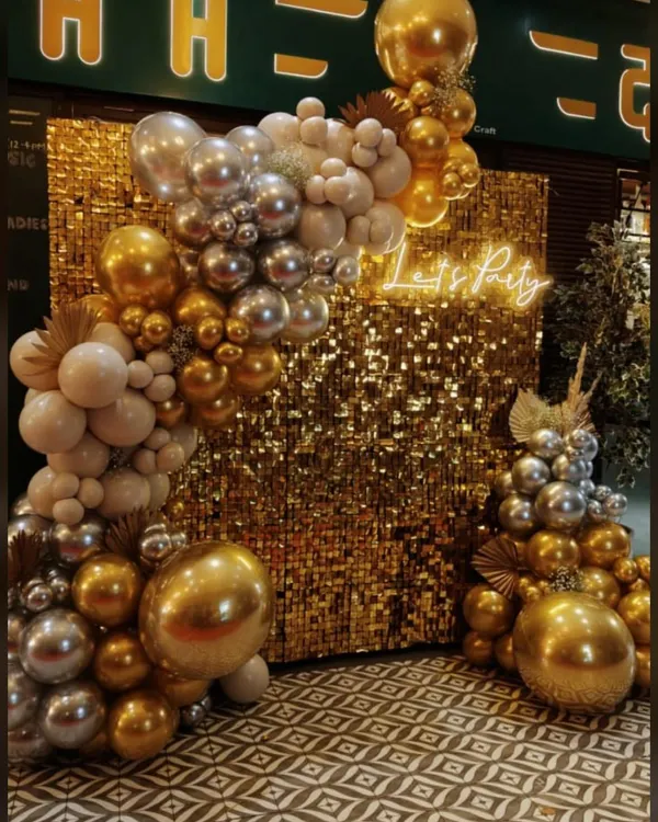 A glamorous photo backdrop combining a gold sequin wall with a metallic gold and silver balloon arch. The "Let's Party" neon sign makes it an instant focal point for any high-energy celebration or corporate gala.