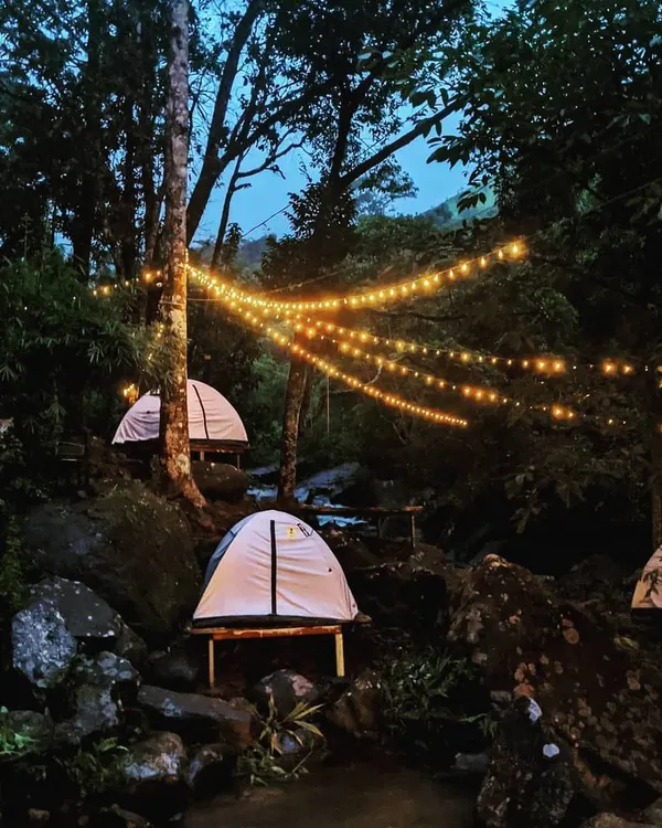 To add a touch of magic to the woods, I often string up warm fairy lights. Here, tents are nestled among the rocks and trees by a stream, creating an enchanting atmosphere as dusk settles in.