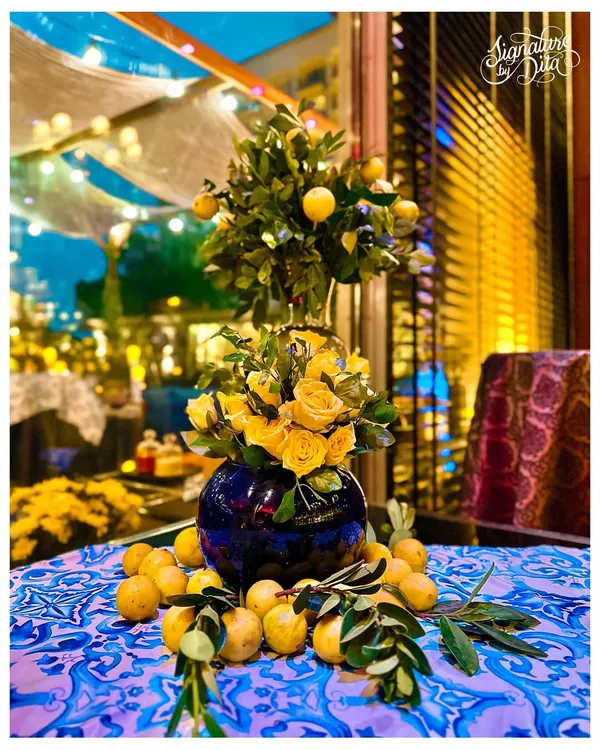 A classic Sicilian tablescape I designed, featuring a vibrant blue and white patterned tablecloth, a centerpiece of yellow roses and a lemon tree, and fresh lemons scattered for a rustic touch.