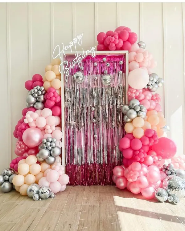 A fabulous photo backdrop made with a shimmering silver curtain and a lush arch of pink and silver balloons, complete with disco balls. The 'Happy Birthday' neon sign adds the final touch.