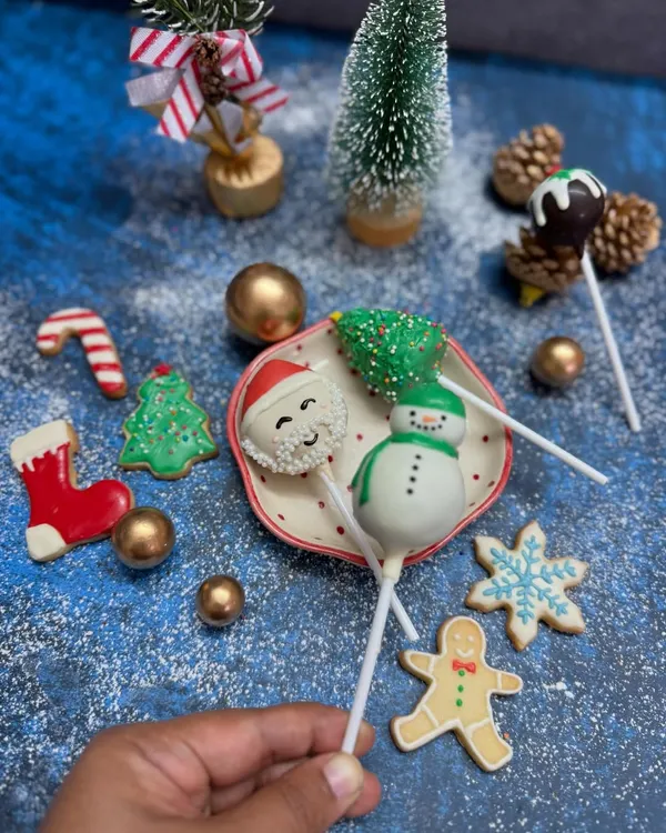 Our Christmas cake pops and cookies are perfect for spreading holiday cheer. This festive flat lay shows our hand-decorated Santa and snowman cake pops alongside an assortment of gingerbread and sugar cookies, ready to be part of your celebrations.