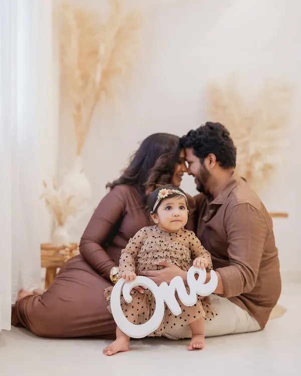 The big number one. This little girl, celebrating her first birthday, sits in front of her parents holding a "One" sign, creating the perfect announcement photo for this special milestone.