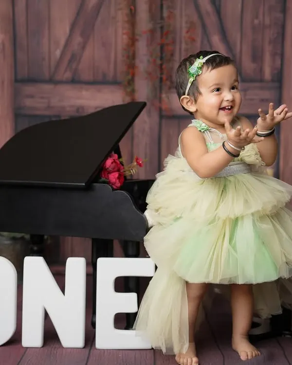 The pure happiness of turning one! This little princess in her beautiful green dress, clapping her hands with joy next to a mini piano, is what first birthday photoshoots are all about.