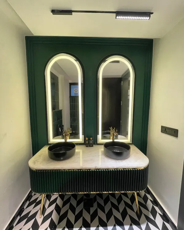 This completed bathroom balances classic and modern elements with its arched, backlit mirrors, a custom green fluted vanity, and striking geometric floor tiles.