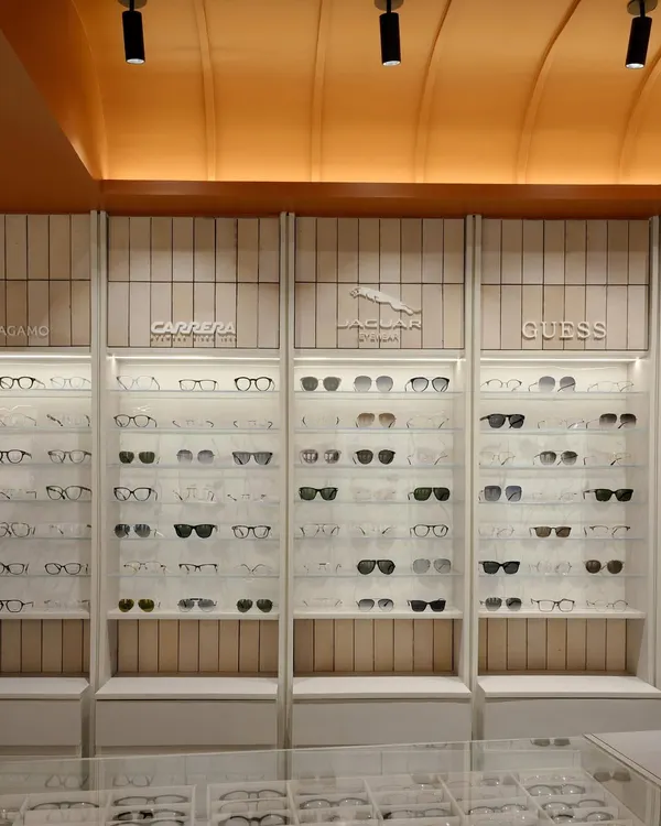The full expanse of the eyewear display at 'The Brick Vault', showing the clean, illuminated shelving set against vertically laid beige tiles, all under the warm glow of the vaulted ceiling.