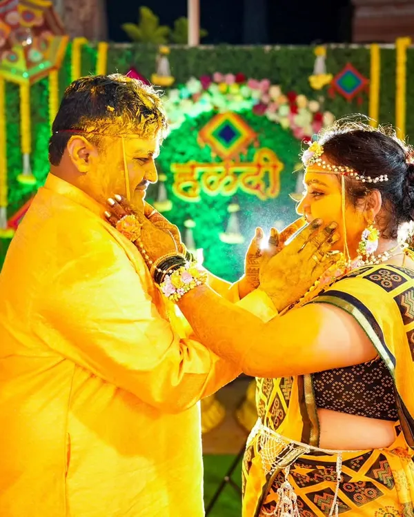 A candid moment during the Haldi ceremony, where the bride and groom lovingly apply turmeric paste to each other against a festive backdrop.