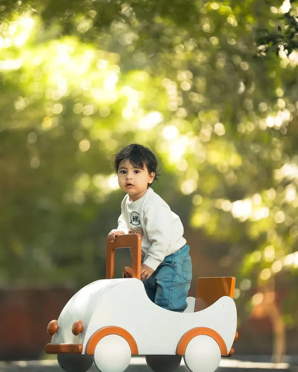 A tiny adventurer on the move. This outdoor portrait uses the beautiful, soft background light, known as bokeh, to make the child and his little toy car pop, creating a magical, sun-drenched image.